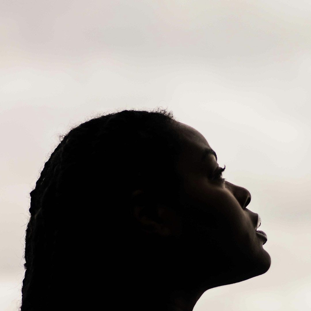 Profile of a person with braided hair against a cloudy sky.